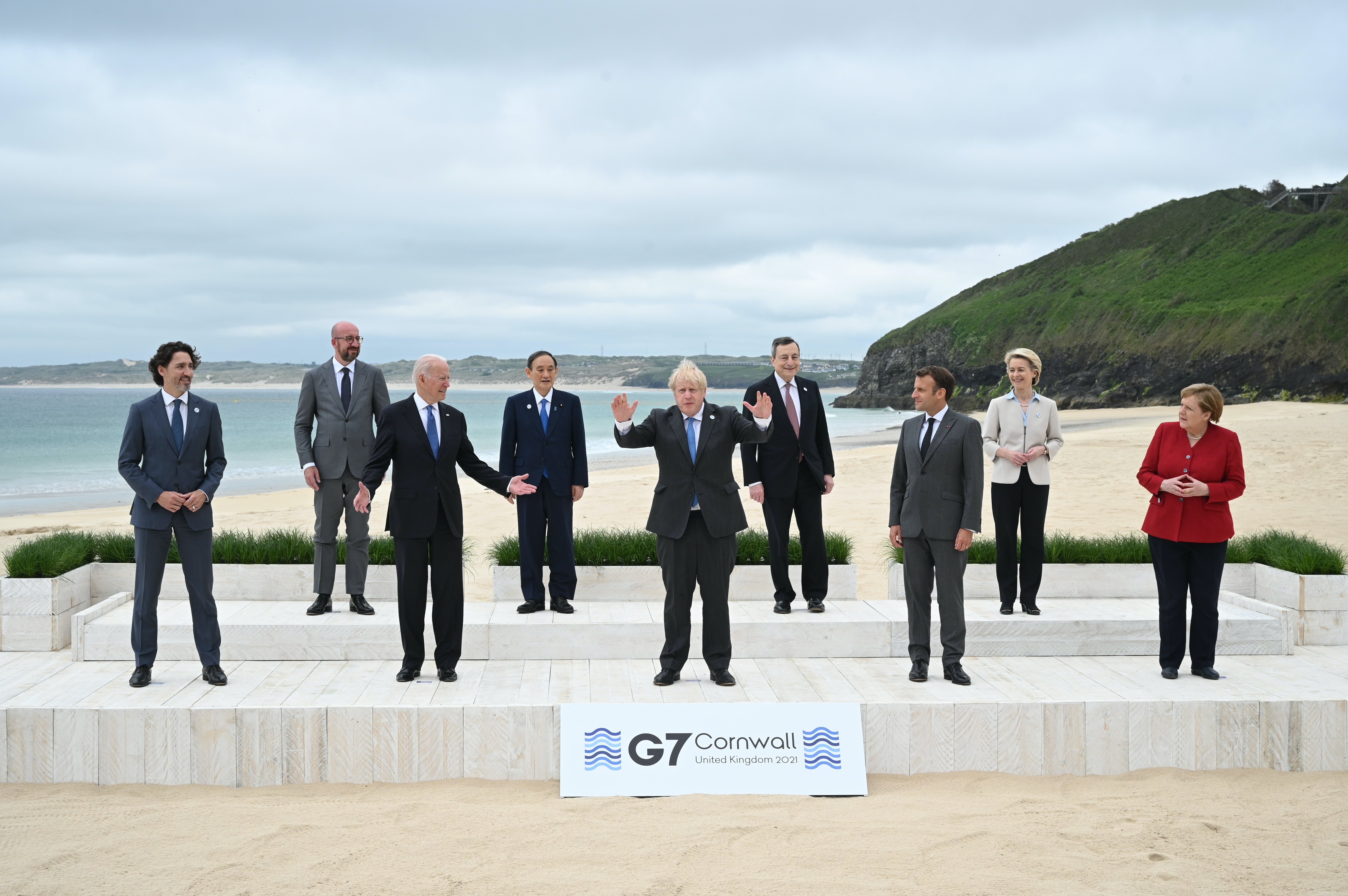 Boris Johnson stands with his arms raised in front of other G7 leaders on a beach.
